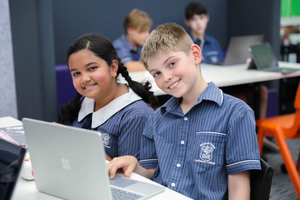princeofpeace-EDIT-5540 Two Prince of Peace Lutheran College students smiling together at a laptop in a co-ed classroom